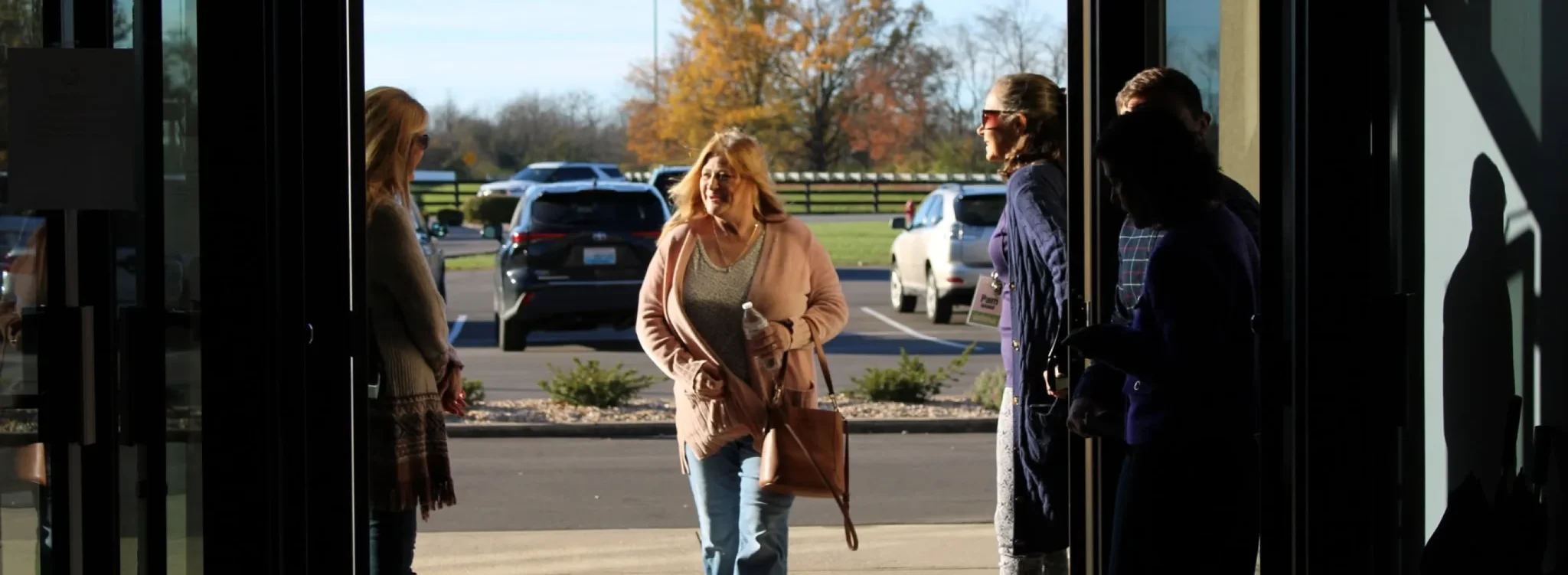 A woman smiles while walking through the church's glass entrance doors as other guests greet each other near the parking lot.