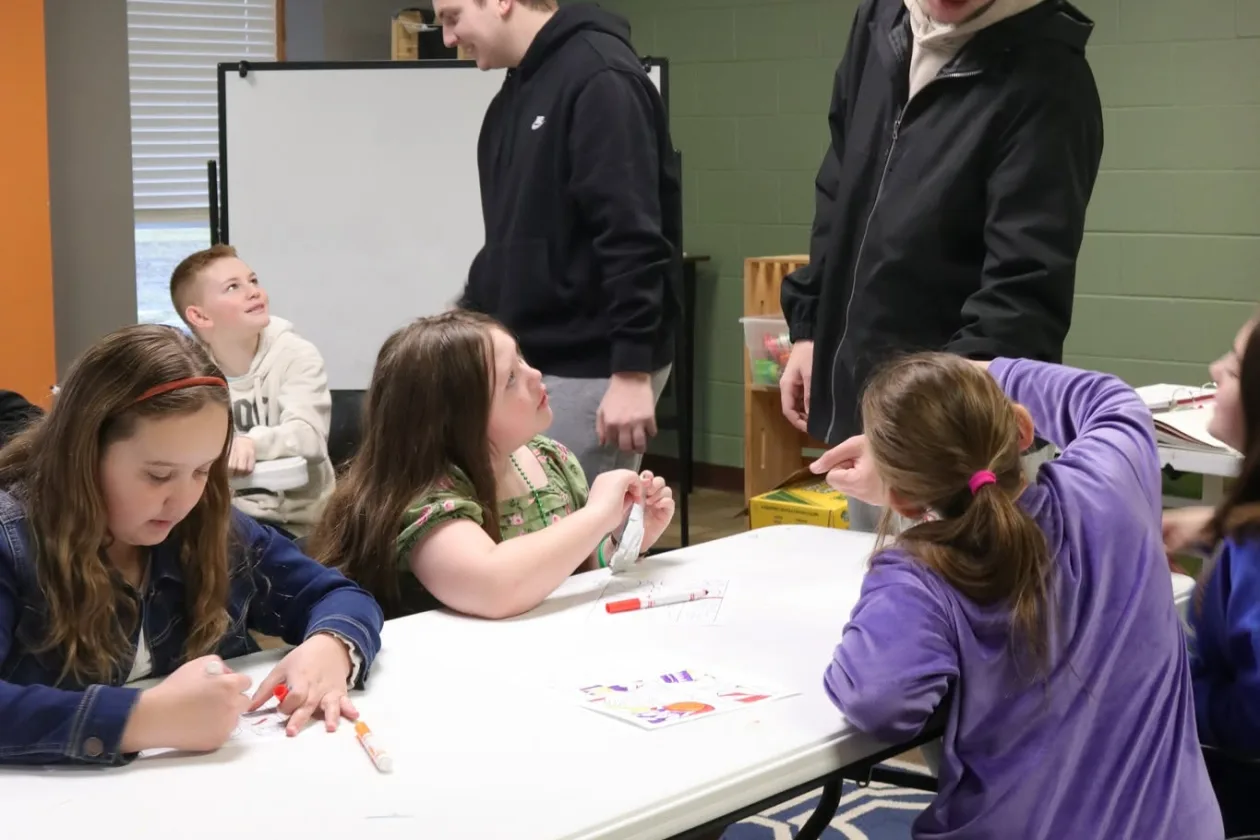 Kids and adult leaders work on an activity together at a table during a Journey Church small group.