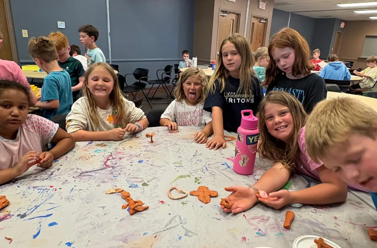 A group of kids gathers around a table making shapes out of modeling dough during a Journey Kids class.