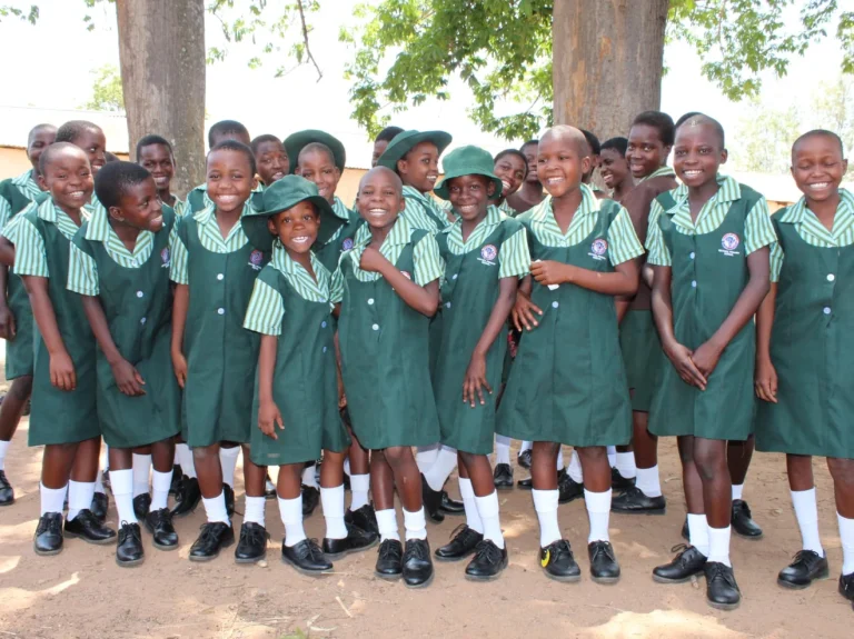 Students in green school uniforms smiling together outdoors at Hippo Valley Christian Mission in Zimbabwe.