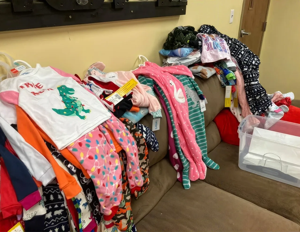 Colorful children's clothing and holiday pajamas are folded and hung around a couch full of donated items at Journey Provisions.