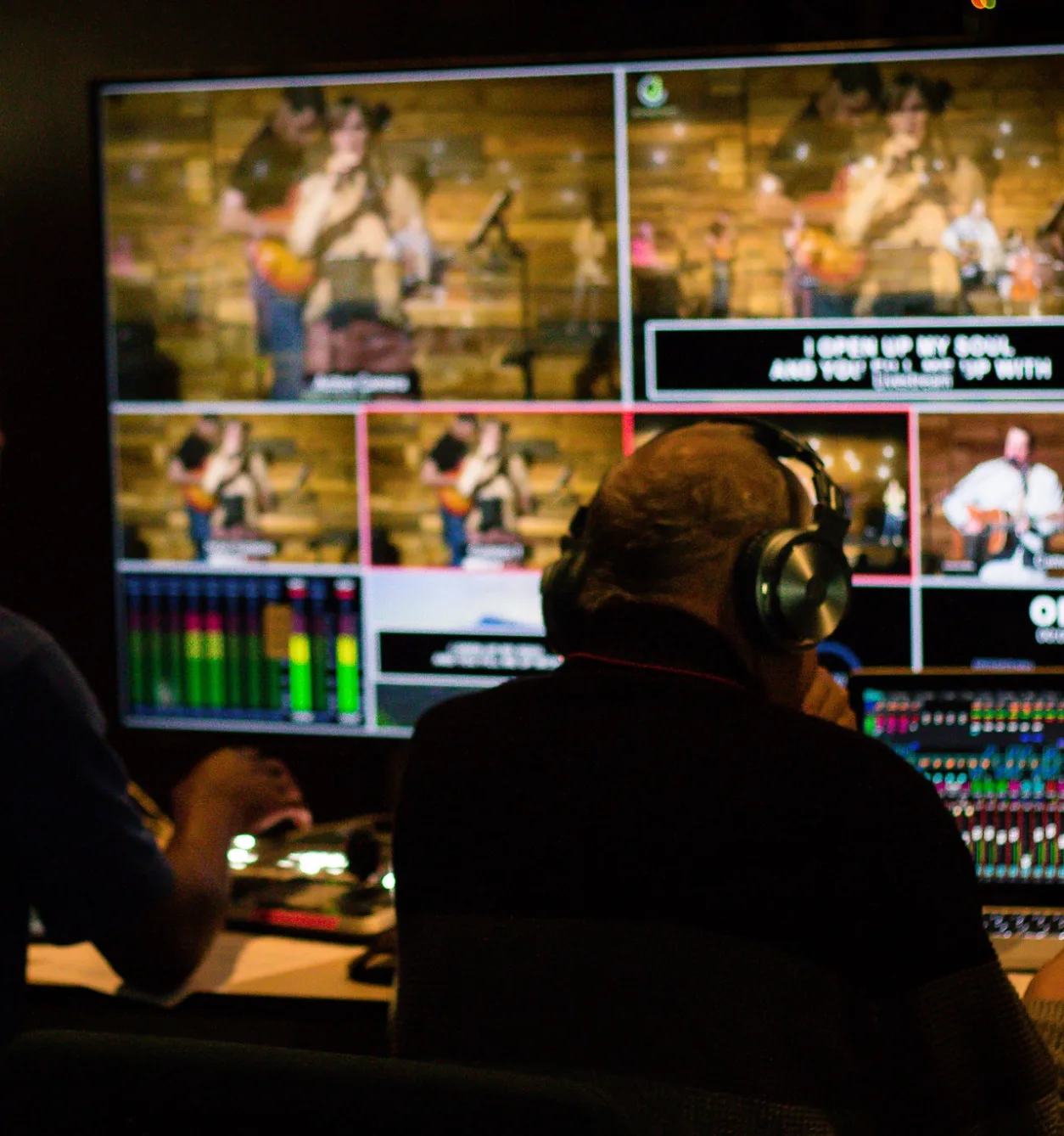 Two volunteers wearing headphones run the video switcher and sound board in the production booth during a Journey Church service.