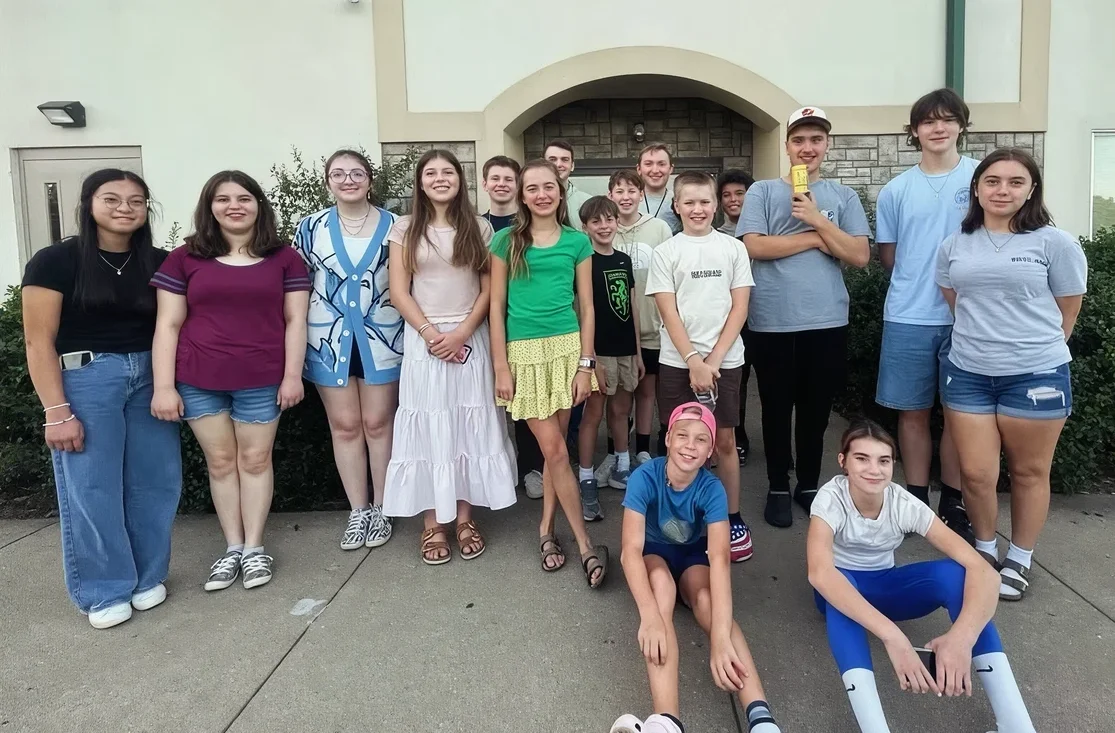 A group of Journey Students teens and volunteers smiling together outside the church building.