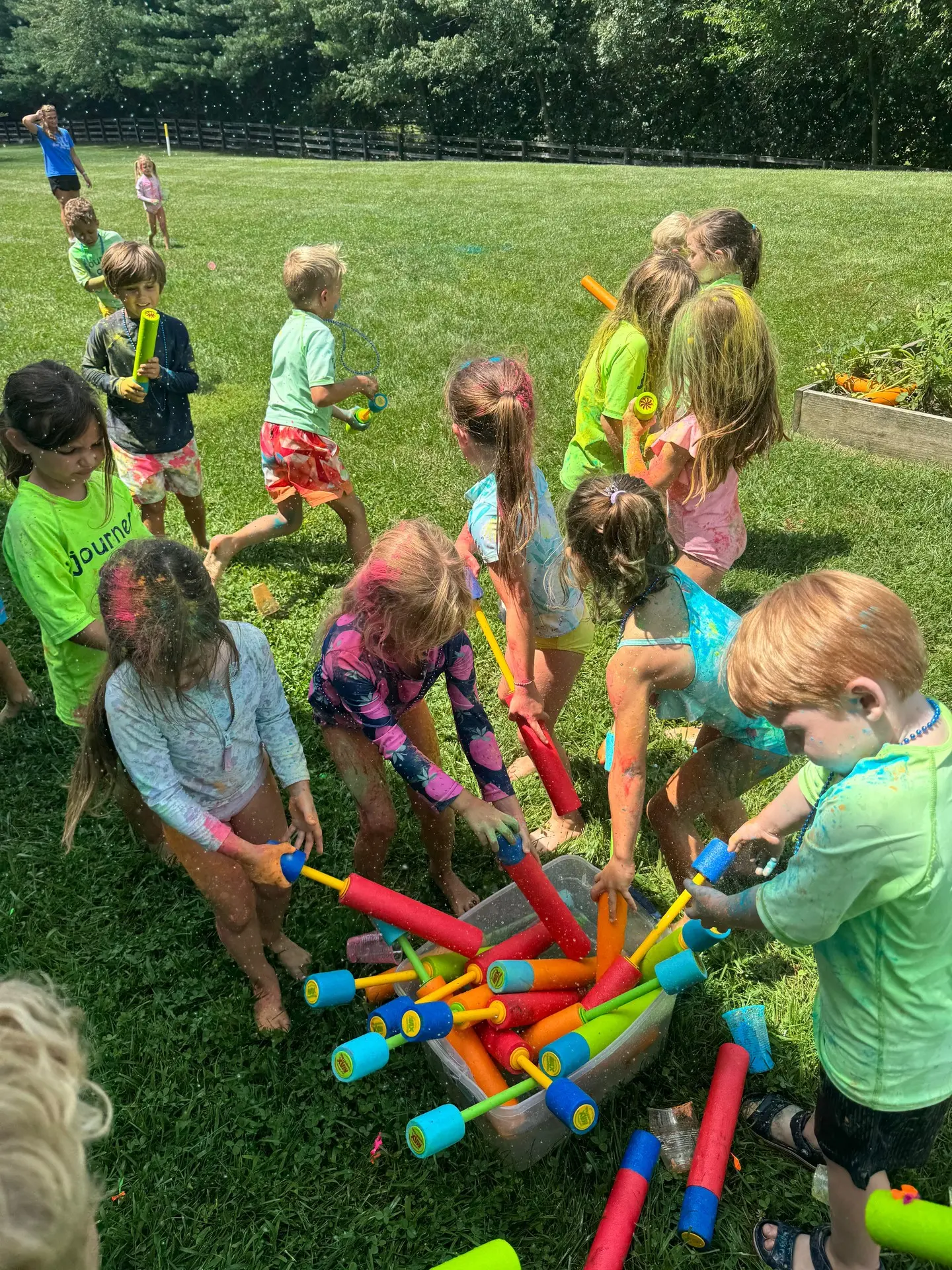 Campers gathered on the grass around a pile of colorful pool noodles during an outdoor camp game