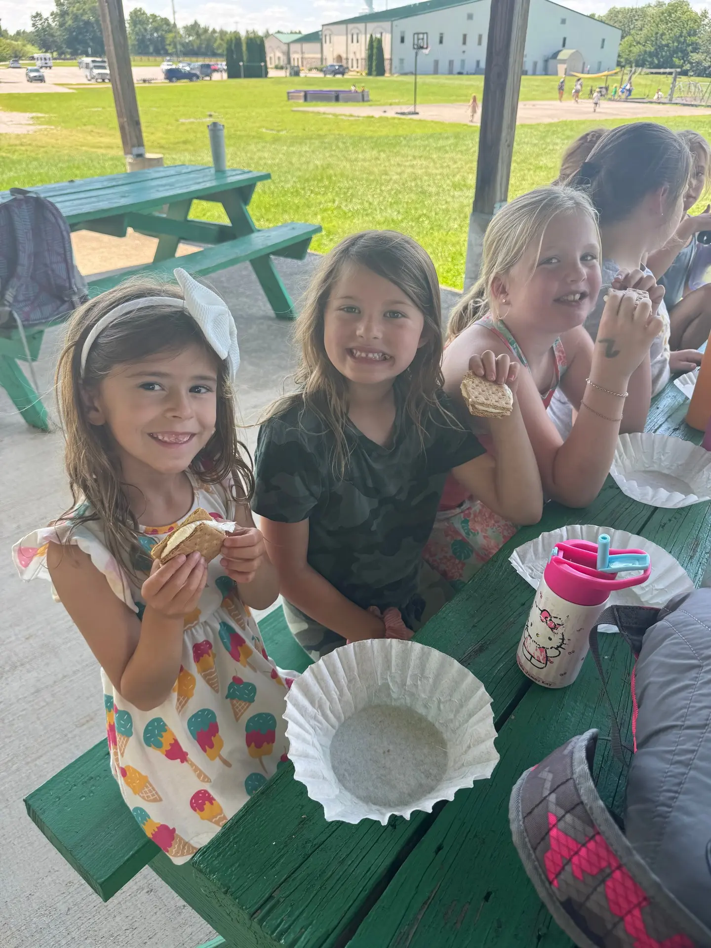 Campers eating snacks together at a green picnic table under an outdoor shelter