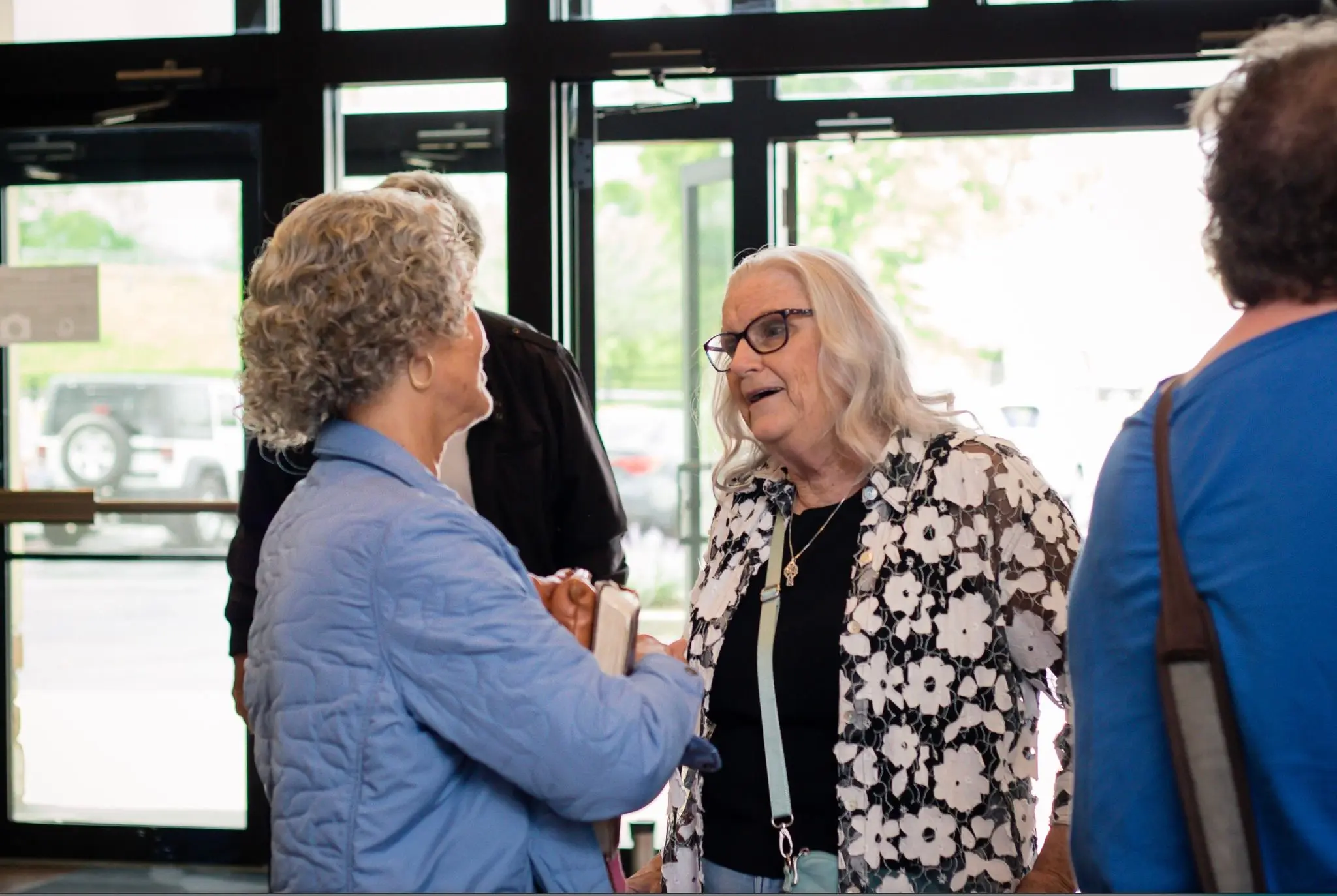 Two women hold a Bible and talk warmly together in the church lobby before service.