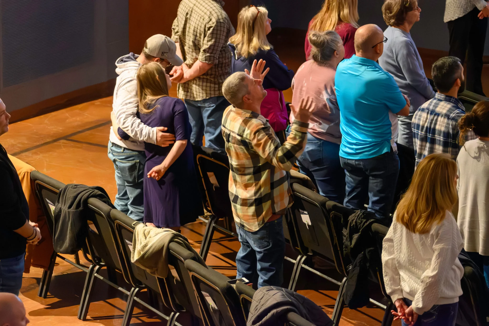 Congregation members raise their hands in worship, with one couple embracing, during a Journey Church service.