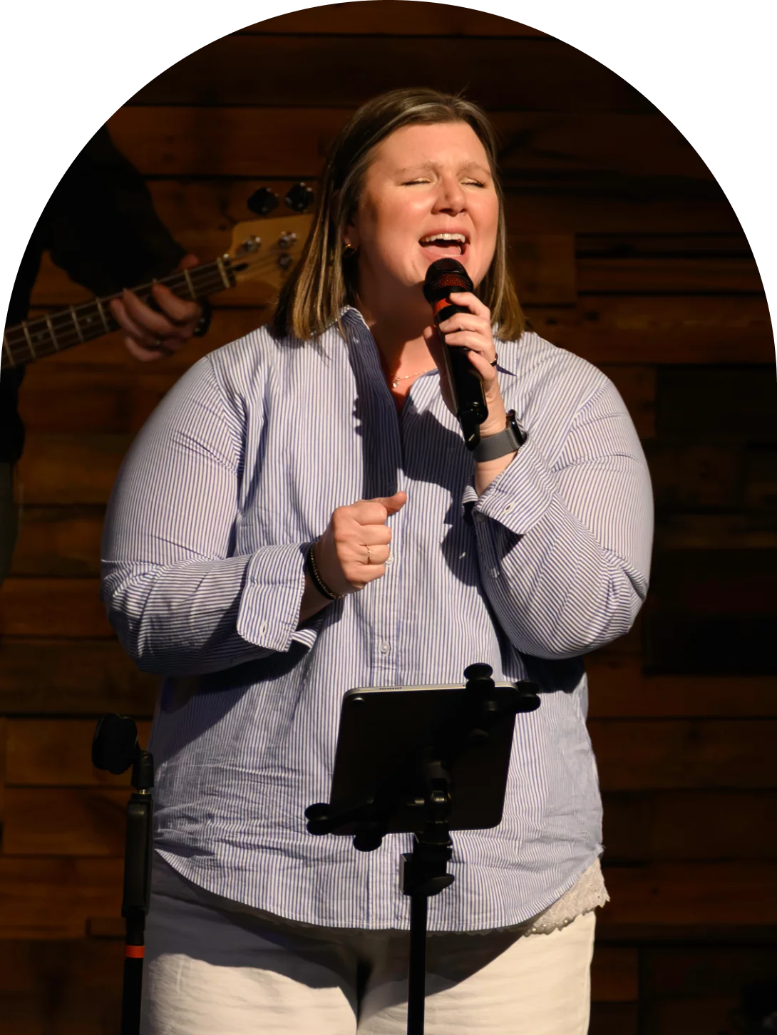 A worship leader sings into a handheld microphone on stage at Journey Church while a bassist plays behind her.