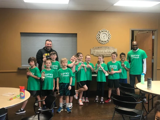 A Journey Hoops team in green jerseys holding their trophies alongside two coaches