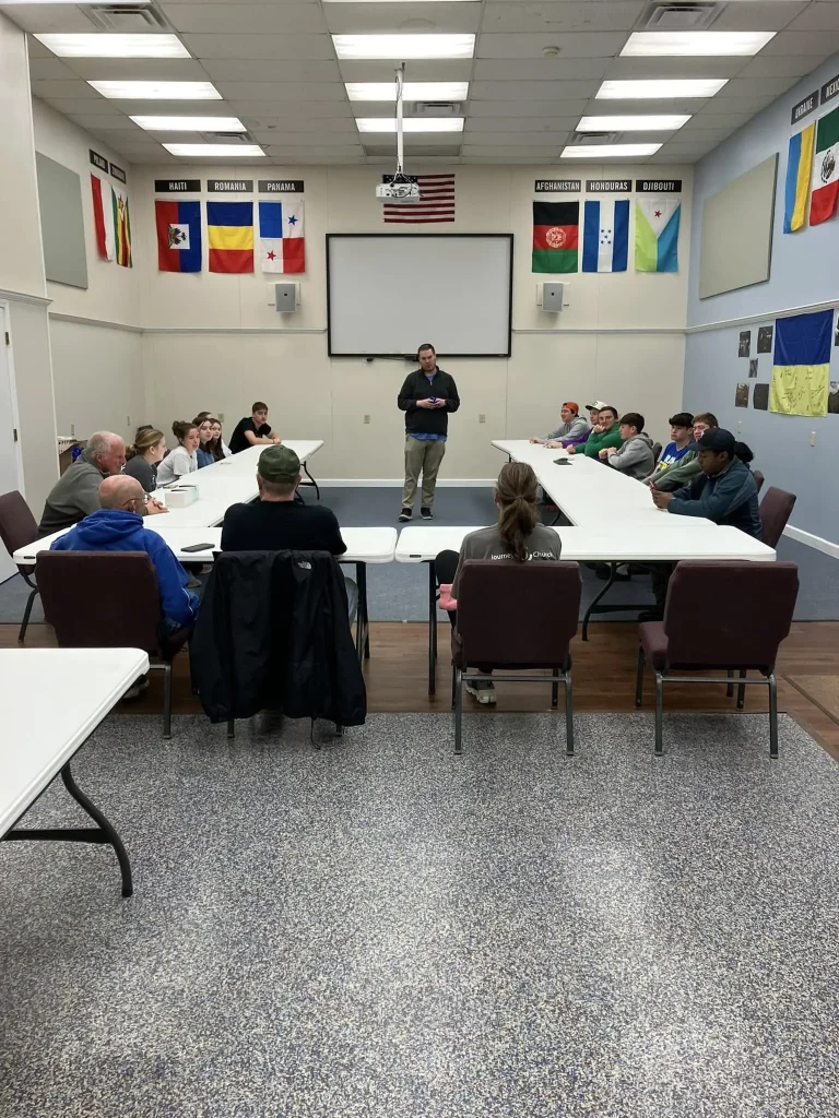 Journey Church members seated at tables during a missions team meeting, with international flags lining the wall