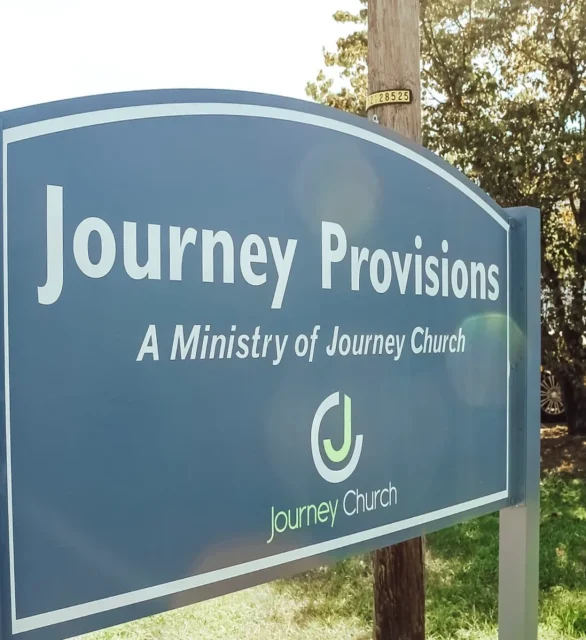 The Journey Provisions roadside sign, reading A Ministry of Journey Church, beside the parking lot.