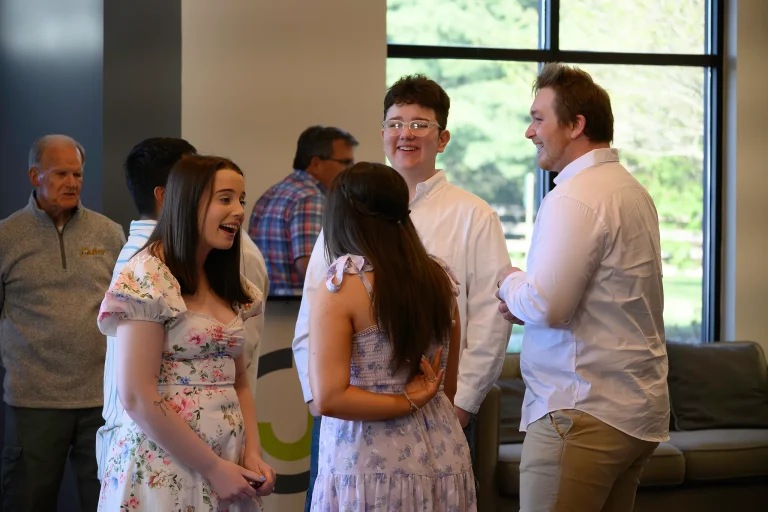 Students and adults talk and laugh together in the Journey Church lobby after an Easter service, with sunlight coming through the tall windows.