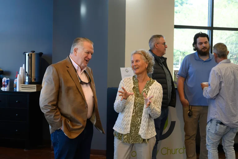Two church members talk and laugh near the coffee station in the Journey Church lobby while others visit in the background.