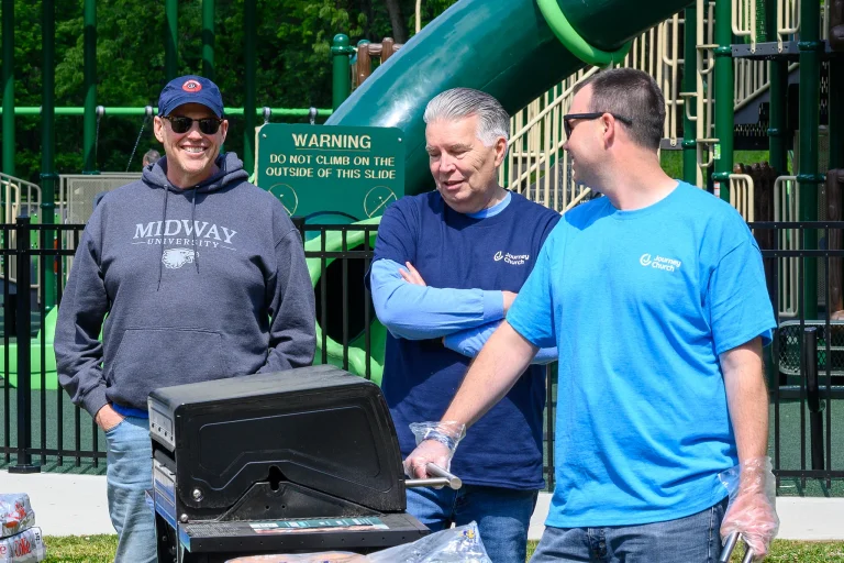 Three volunteers in Journey Church shirts grill out beside the playground during a church event.