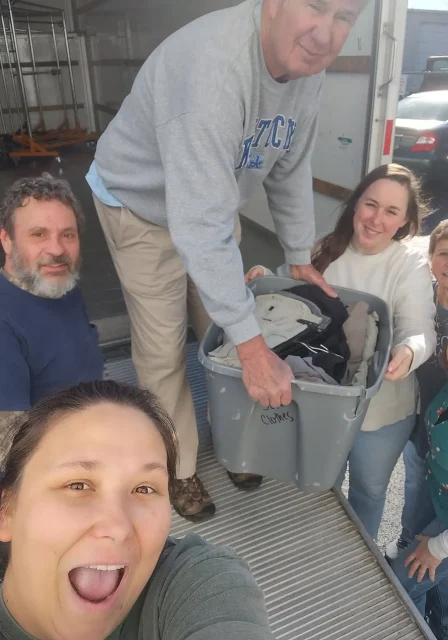 Volunteers unloading bins of donated clothing from a truck, one of them taking a selfie