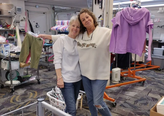 Two volunteers standing together among racks of donated clothing at Journey Provisions