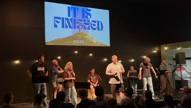 A student worship band leading from the stage with "It Is Finished" displayed on the screen behind them
