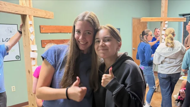 Two students giving a thumbs up beside a wooden cross at a student event