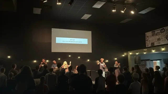 Students standing in a dim auditorium as the worship team leads from the stage
