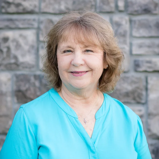 Joni Edester, Preschool Director at Journey Preschool, smiling in a teal top in front of a stone wall.