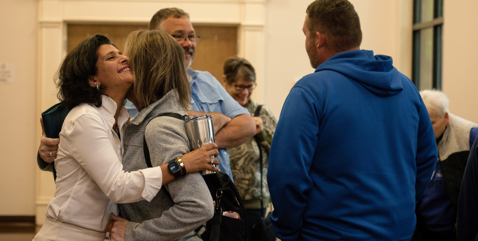 Two women embrace and greet each other warmly inside the church lobby.